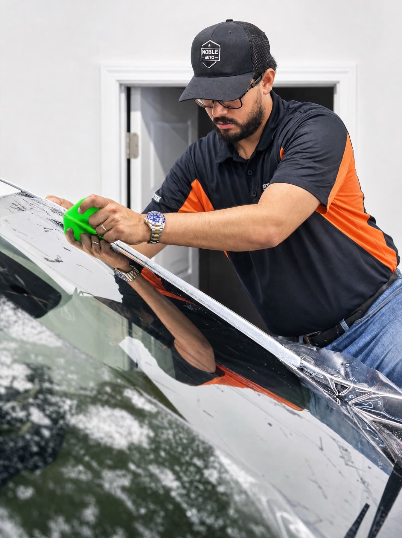 Noble Auto technician hand-squeegeeing freshly laid film across a windshield